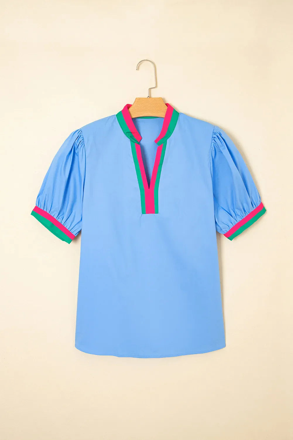 Blue blouse with colorful trim on a hanger against a beige background