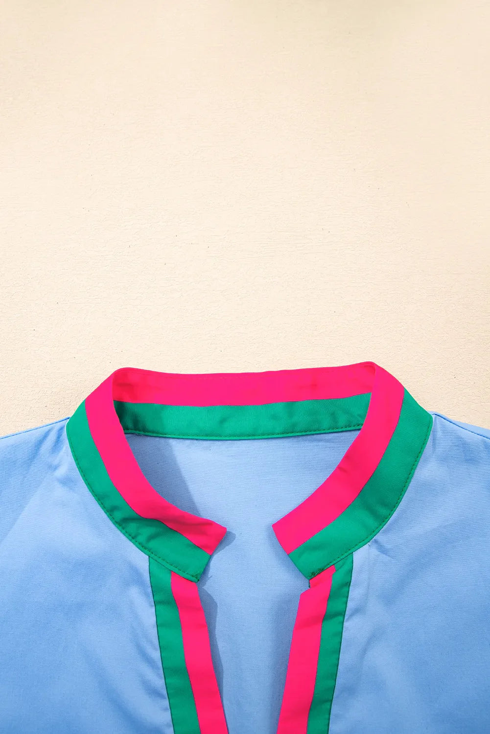 Close-up of a blue shirt with pink and green collar on a beige background