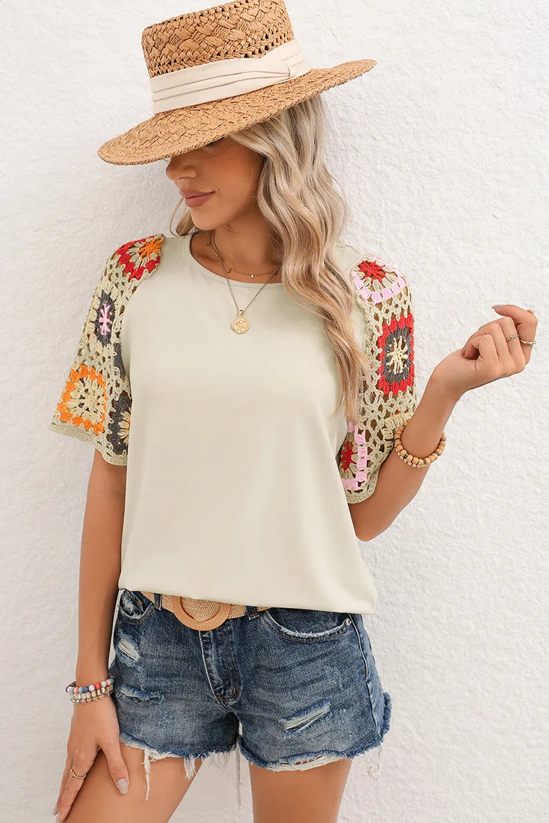 Woman wearing a white top with colorful sleeves, denim shorts, and a straw hat against a white background
