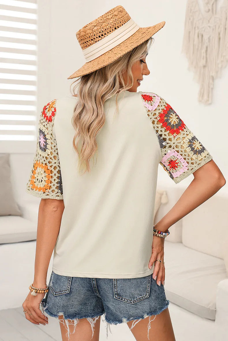 Woman wearing a beige top with floral sleeves and denim shorts indoors.