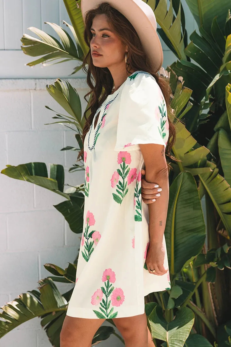 Woman wearing a white dress with pink floral patterns in a tropical setting.
