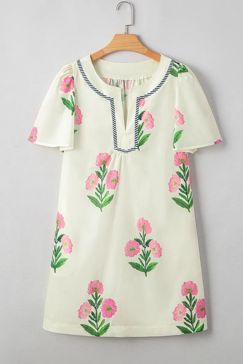 White dress with pink floral embroidery on a hanger against a gray background