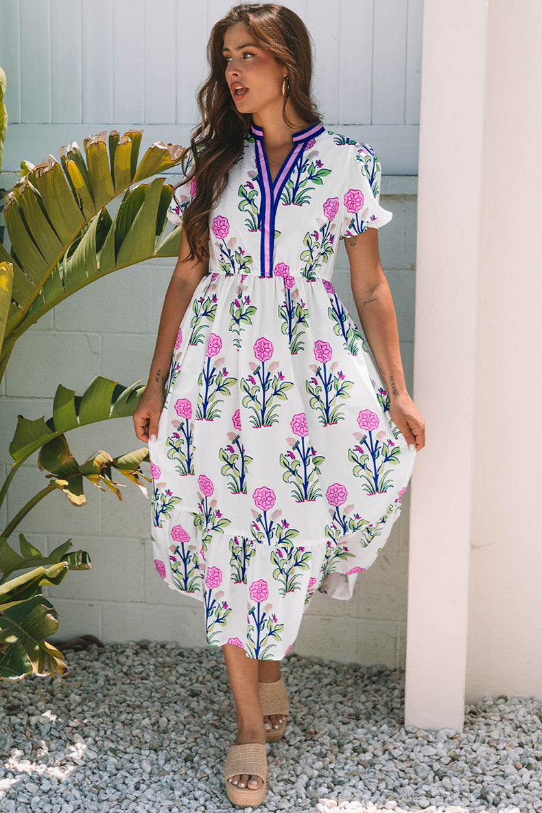 Woman wearing a floral dress standing outdoors with plants and a white wall in the background