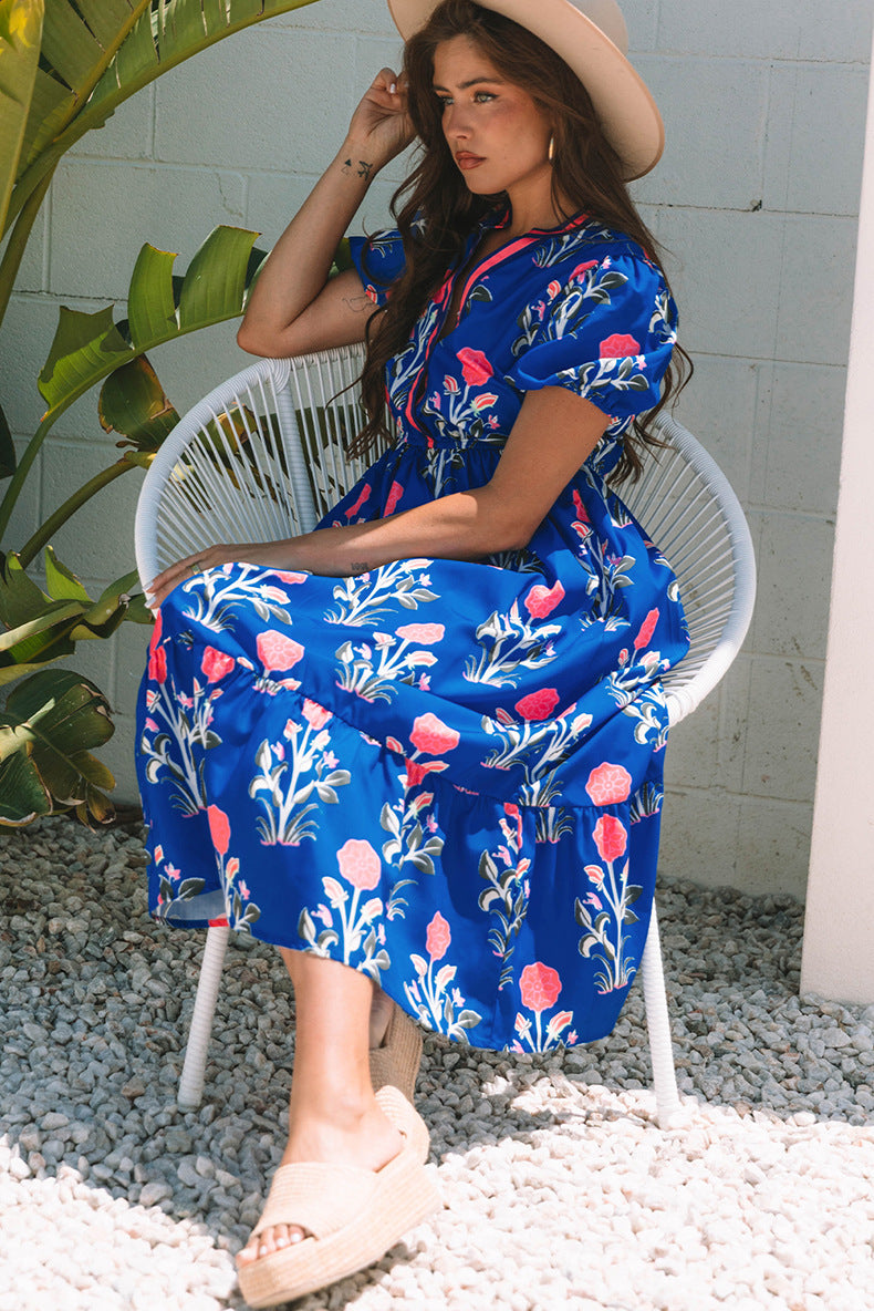 Woman in a blue floral dress sitting on a white chair outdoors.