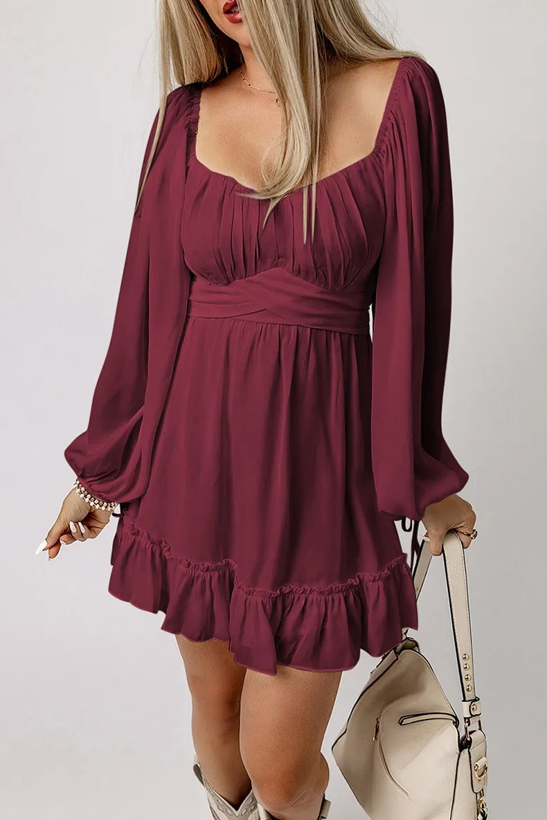 Woman wearing a burgundy dress with long sleeves and ruffled hem, holding a beige handbag.
