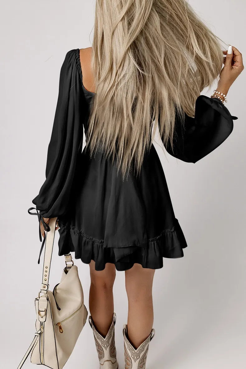 Person wearing a black dress with ruffled sleeves and hem, standing against a plain background.