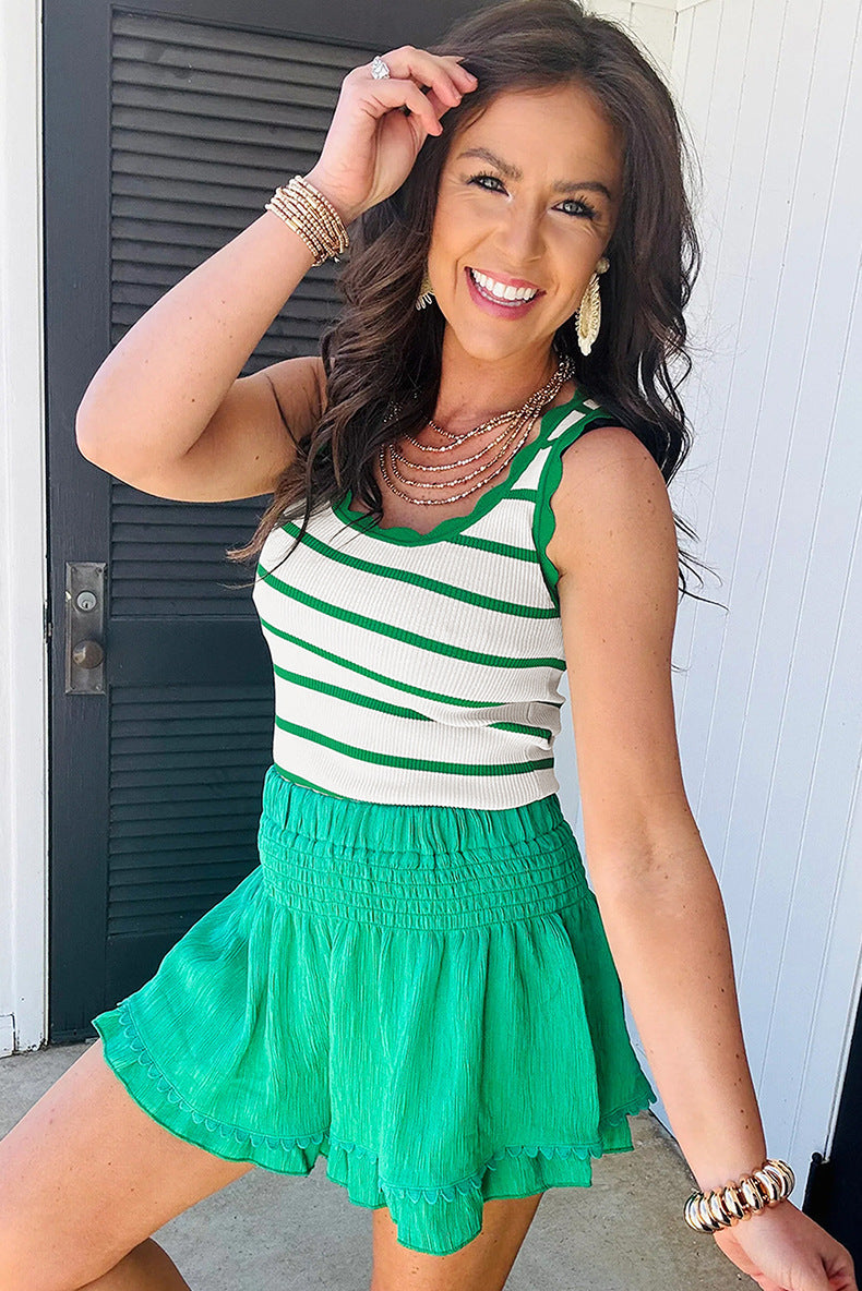 Woman wearing a green and white striped top with a green skirt, standing against a white wall.