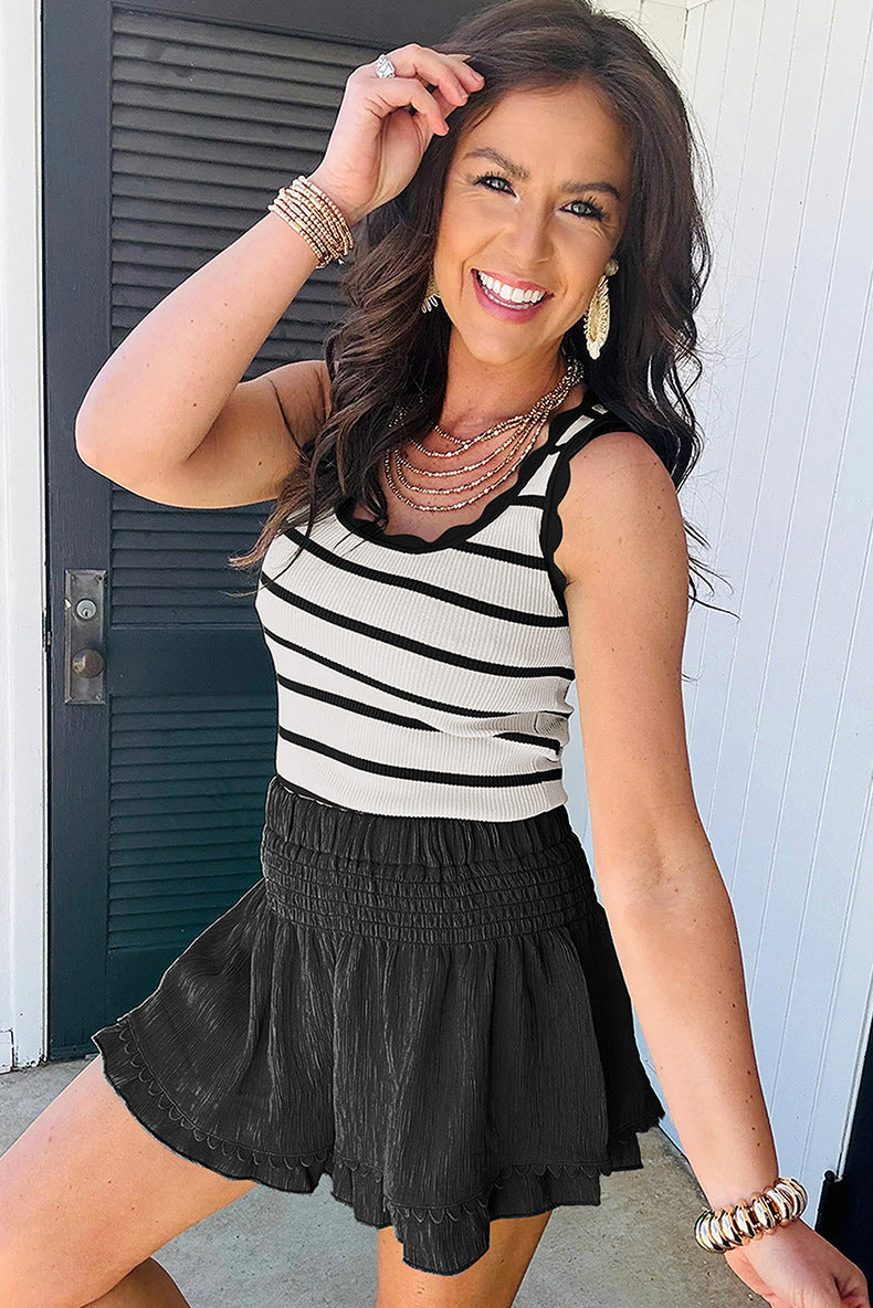 Woman wearing a black and white striped tank top and black skirt, standing against a white wall.